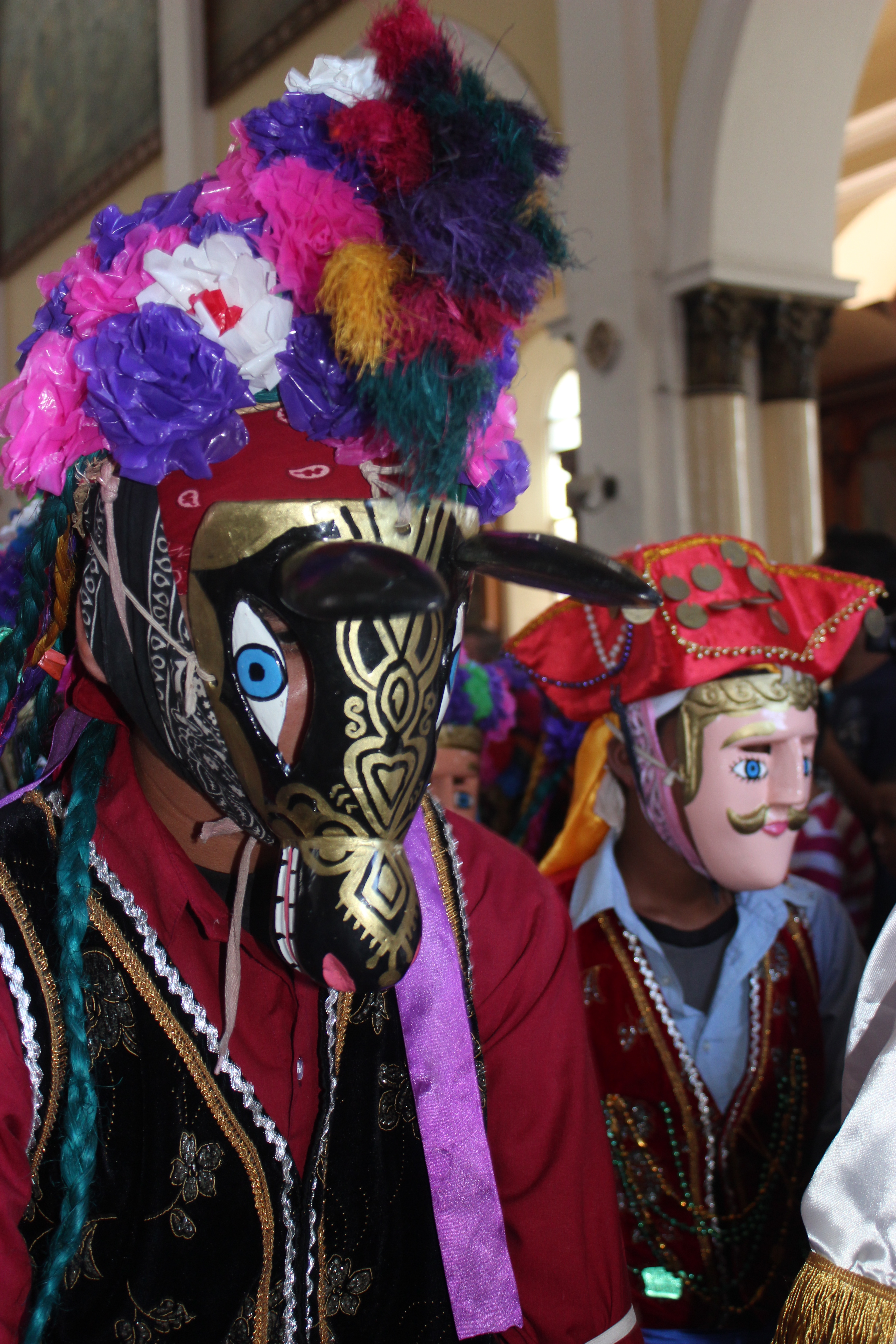 The picture show a man wearing a really huge mask and behind him there's another man wearing a mask of an old man.